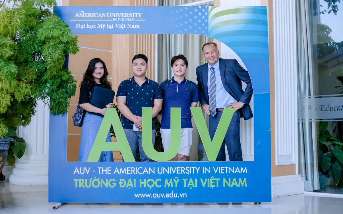 Three AUV students and a faculty member smiling behind the AUV sign