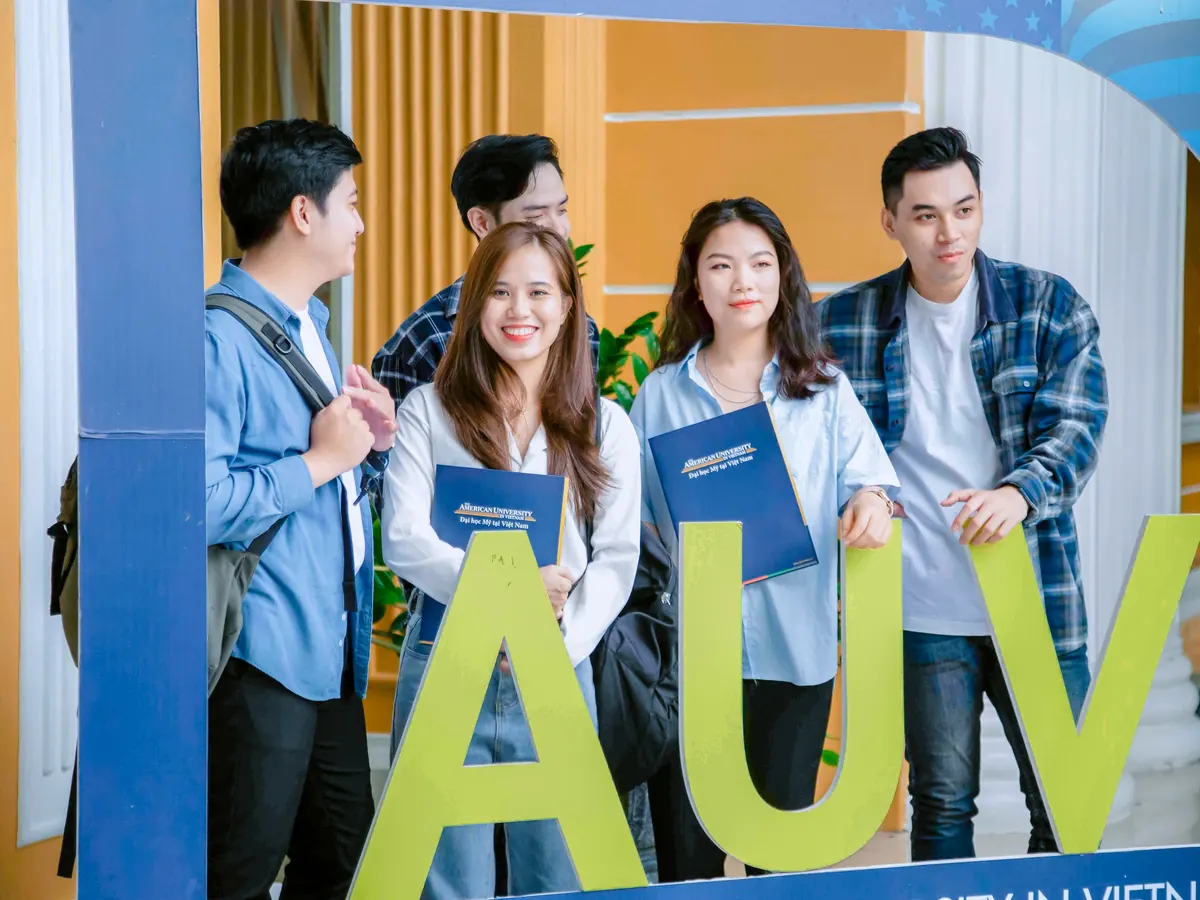 Five AUV students smiling behind large AUV letters on campus