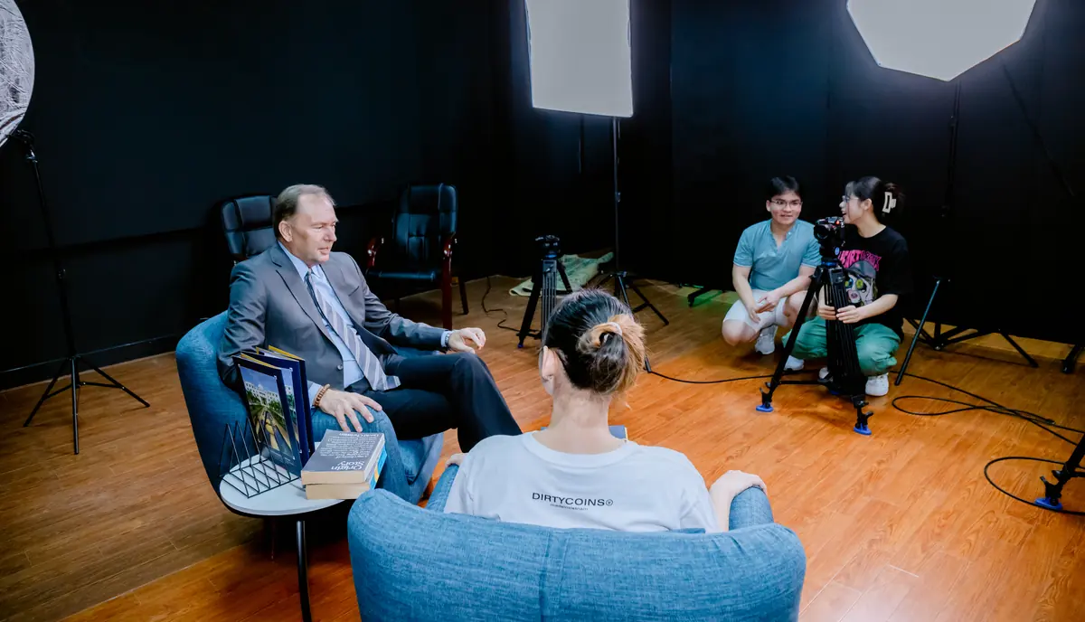 A student interviews a guest while classmates run the camera